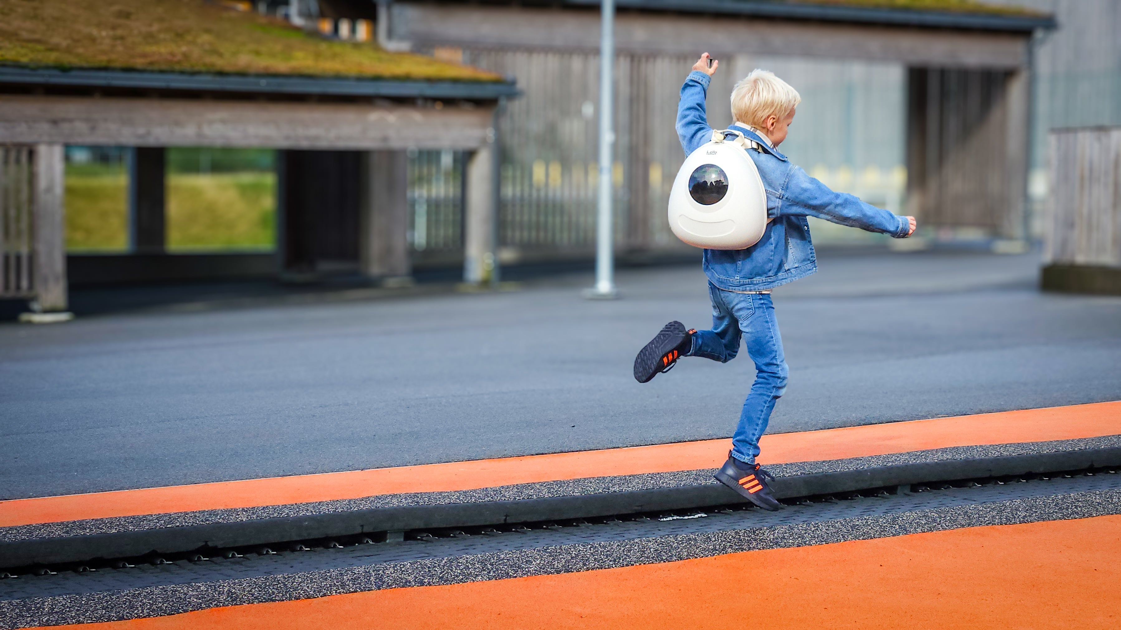 Boy in denim outfit jumping on a trampoline while wearing a Whipped Cream White Ledback Buddy backpack with a round LED screen.
